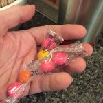 Hand holding 3 packets of cellophane-wrapped round candies.